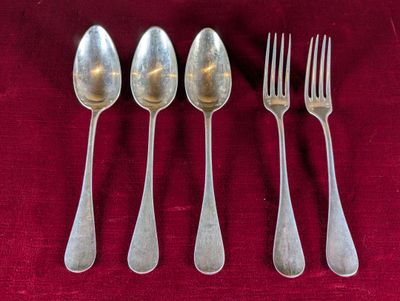 quatre cuillères en argent et une fourchette posées sur une nappe rouge