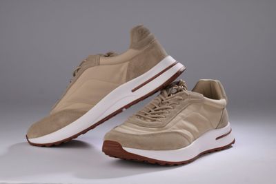 une paire de baskets beiges à semelles blanches sur fond gris
