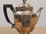 une théière ancienne en argent posée sur une table en bois, dotée d'une poignée noire