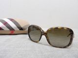 burberl sunglasses and a case on a bed with a white background