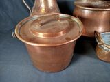 three copper pots and a copper jug on a black background