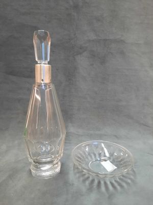 a glass bottle with a silver lid next to a glass ashtray