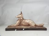 statue of a dog laying down on a wooden base on a white background
