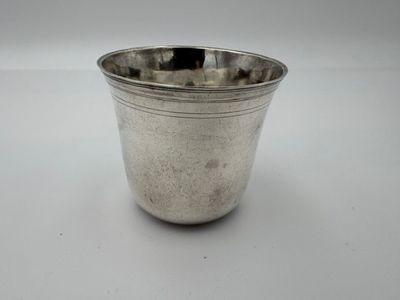 une vieille coupe en argent munie d'une anse, posée sur une surface blanche