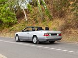 a silver convertible car driving down the road with trees in the background