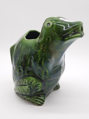a green frog vase sitting on a white surface
