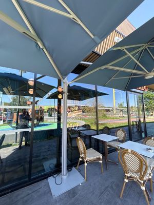 des tables et des chaises sous des parasols, sur une terrasse avec une piscine en arrière-plan