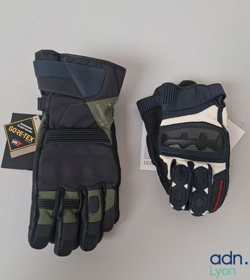 une paire de gants de moto noirs et verts posés sur une surface blanche