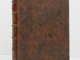 an old book with a brown cover sitting on a white surface