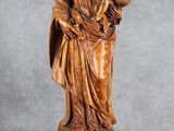 une statue en bois représentant une femme tenant un enfant dans ses bras, posée sur un socle