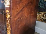 a wooden chest of drawers in a room with a floral wallpaper behind it