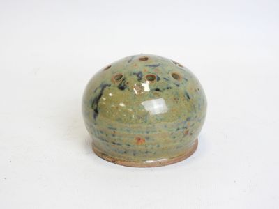 a small green vase with holes in it on a white surface