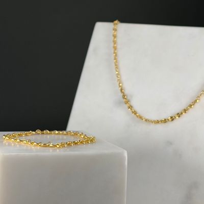 a close up of a gold necklace and bracelet on a marble block
