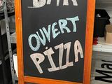 une pancarte indiquant « Bar Overt Pizza » posée par terre