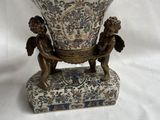 un vase orné de deux chérubins, posé sur un socle