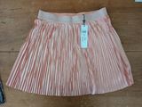 pink pleated skirt on a wooden floor next to a pair of jeans