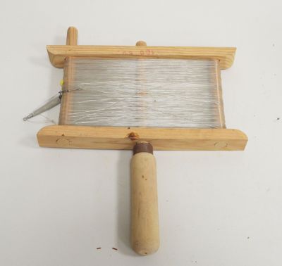 un petit métier à tisser muni d'une poignée en bois, posé sur une surface blanche