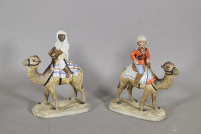 deux figurines représentant des personnes à dos de chameau, posées sur un fond gris