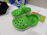 pair of green crocs on a table next to a pair of black shoes