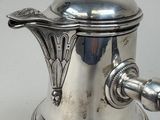 a silver coffee pot with a handle on a table