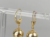 une paire de boucles d'oreilles en forme de boules dorées, présentées sur un support en plastique transparent