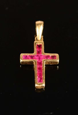 a close up of a gold cross with pink stones on a black surface