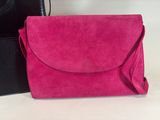 the pink sued clutch bag is next to the black leather purse