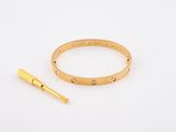 a close up of a gold bracelet and a gold pin on a white surface
