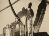 une photo en noir et blanc représentant trois bouteilles et une plume posées sur une table