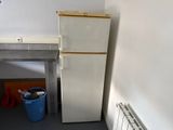 a refrigerator in the corner of a room next to a trash can