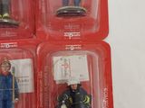 six figurines of firemen in plastic cases on a white surface