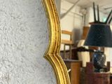 a gold mirror hanging on the wall next to a lamp