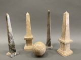 un obélisque en trois pierres et une boule de marbre posée sur une surface grise