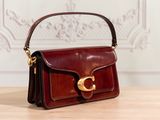 brown leather handbag with gold hardware on wooden table in front of white wall