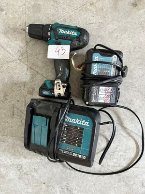 une perceuse filaire et deux batteries posées par terre