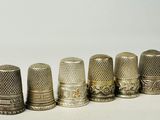 six antique thimbles lined up in a row on a white surface