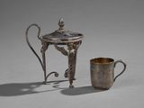 théière et tasse plaquées argent posées sur une table devant un fond gris