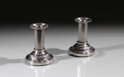 une paire de bougeoirs en argent posés sur une surface blanche, sur fond noir