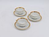 three cups and saucers with gold rims on a white surface