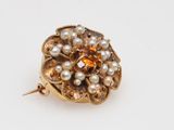 a close up of a gold brooch with pearls and a stone