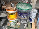 several buckets of paint are stacked on a pallet in a garage