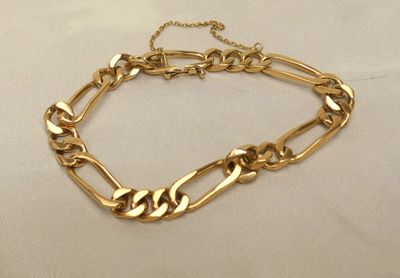 gros plan d'un bracelet en chaîne en or sur une surface blanche