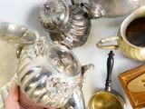 une personne tenant une tasse de café à côté d'une théière en argent