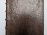 un vieux livre brun posé sur une table à côté d'un mur blanc