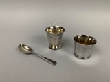 deux tasses en argent et une cuillère posées sur une table