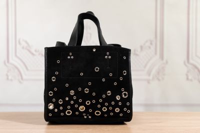 sac cabas noir clouté posé sur une table en bois devant un mur