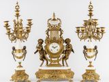 une horloge en or posée sur une table, à côté de trois lustres