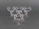 six verres à vin transparents sont disposés en triangle sur une surface grise