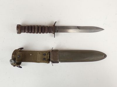 pair of military knifes on a white surface with a leather sheath