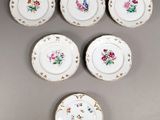 six petites assiettes ornées de motifs floraux sont disposées sur un fond gris